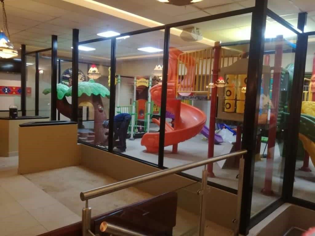 Play area at a restaurant, enclosed by glass. Slides and climbing structures in bright colors.