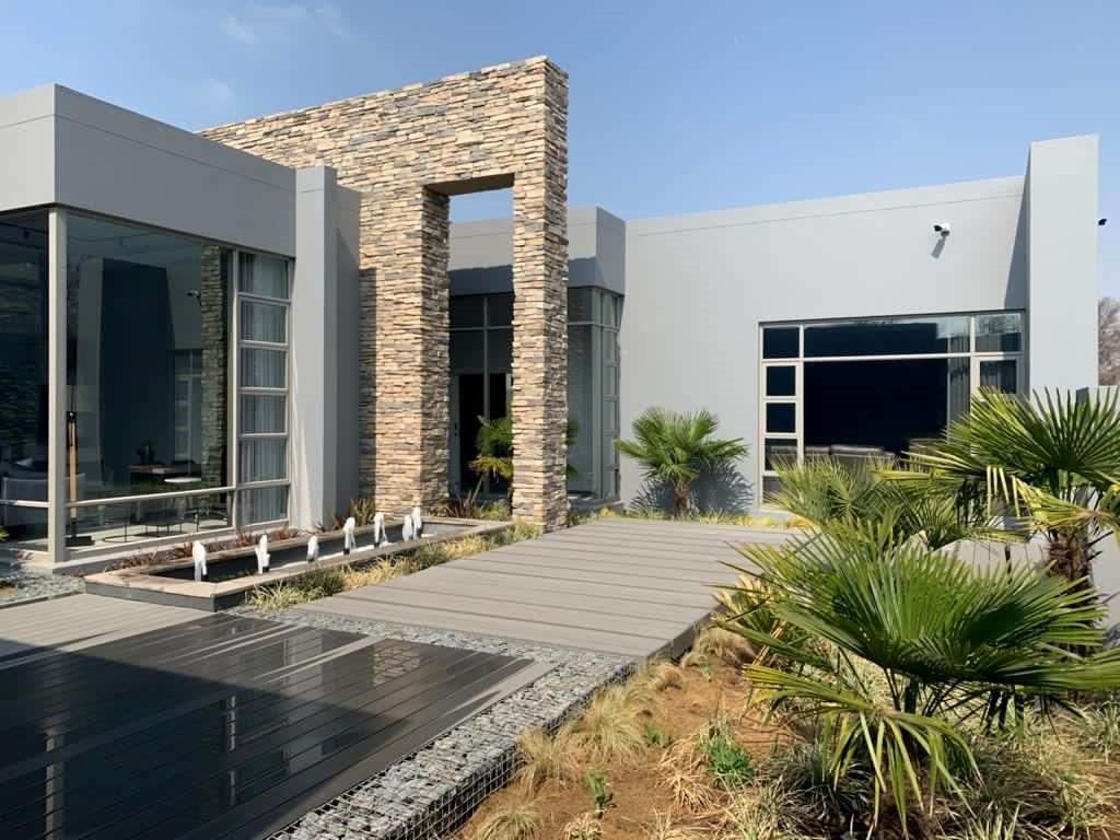 Modern gray house with stone accent and water feature; sunny day.