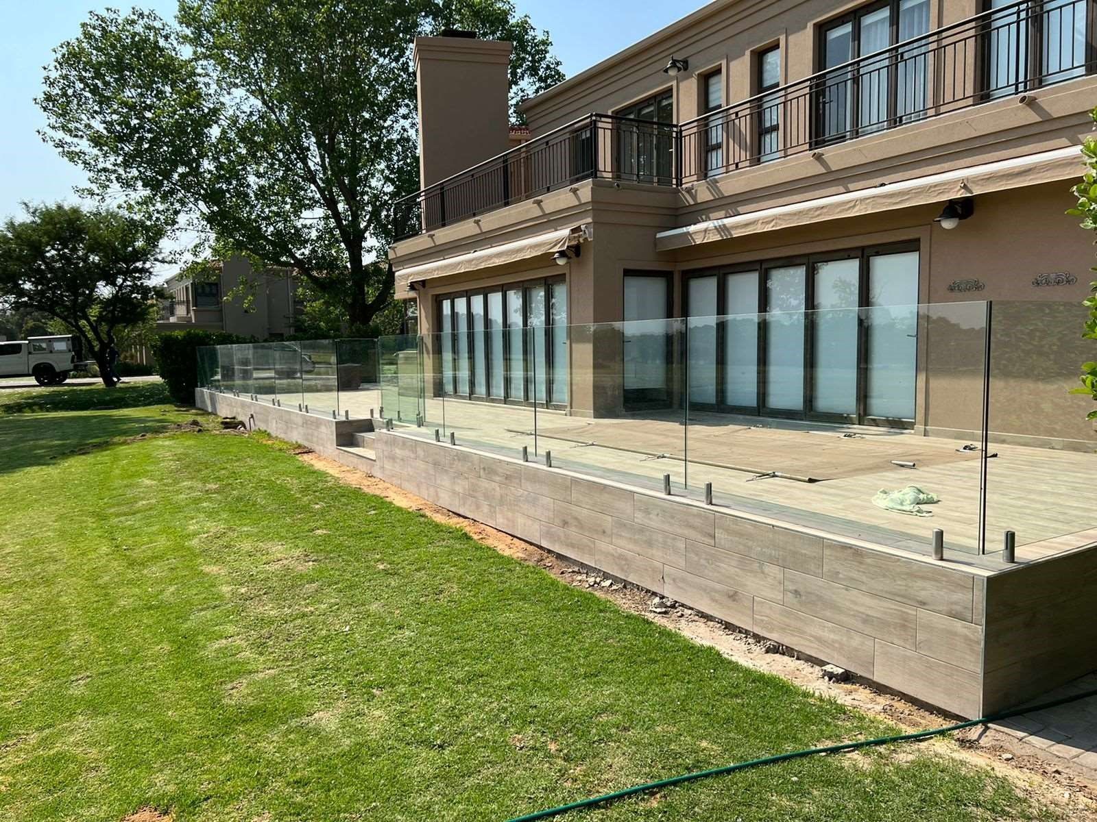 A modern home with glass balcony railings, green grass, and a sunny exterior.