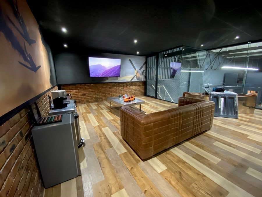 Living room with leather sofa, TV, and brick accent wall; warm tones.