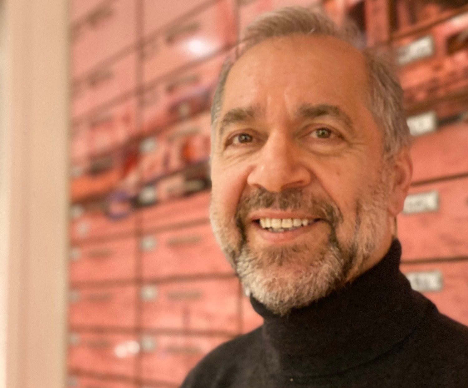 Een man met een baard en een zwarte coltrui lacht naar de camera