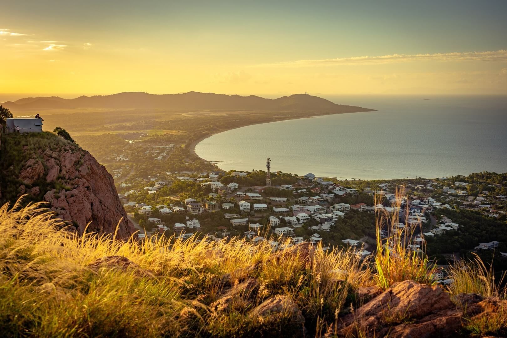 A view of a city from a hill overlooking the ocean at sunset.
