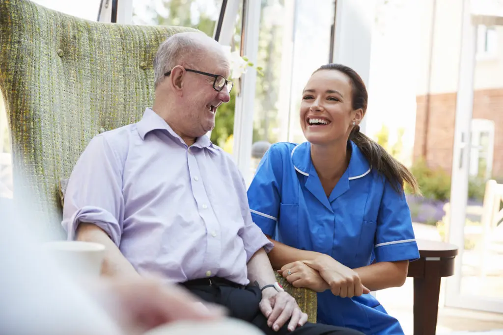 A nurse is holding the hand of an elderly man in a chair.