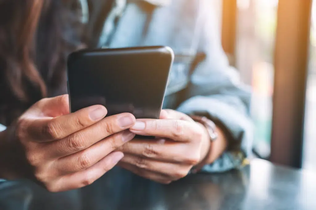 A woman is sitting at a table using a cell phone.