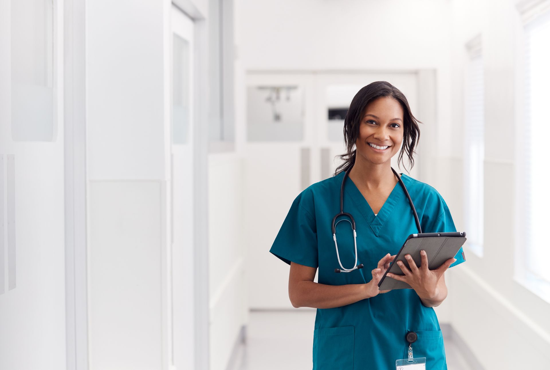A nurse is holding a tablet in a hospital hallway.