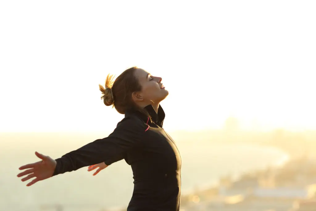 A woman is standing on the beach with her arms outstretched.