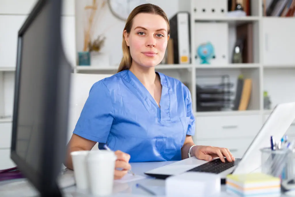 A nurse is sitting at a desk using a laptop computer.