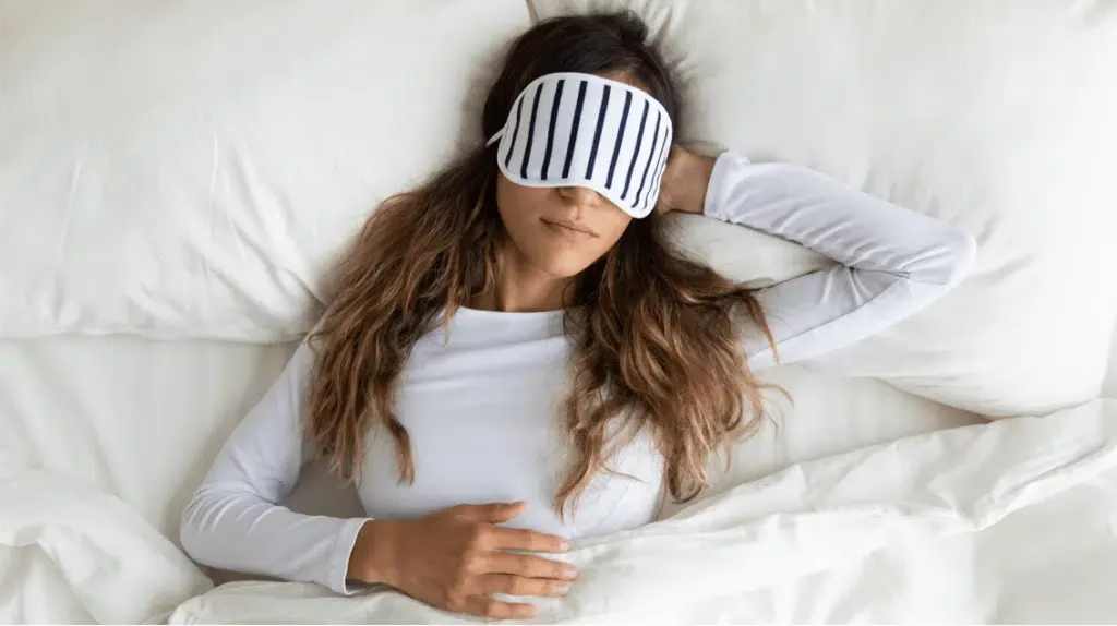 A woman is sleeping in bed with a sleep mask on her eyes.