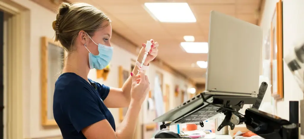 A nurse wearing a mask is preparing an injection in a hospital.
