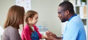 A doctor is examining a little girl 's arm while a woman looks on.