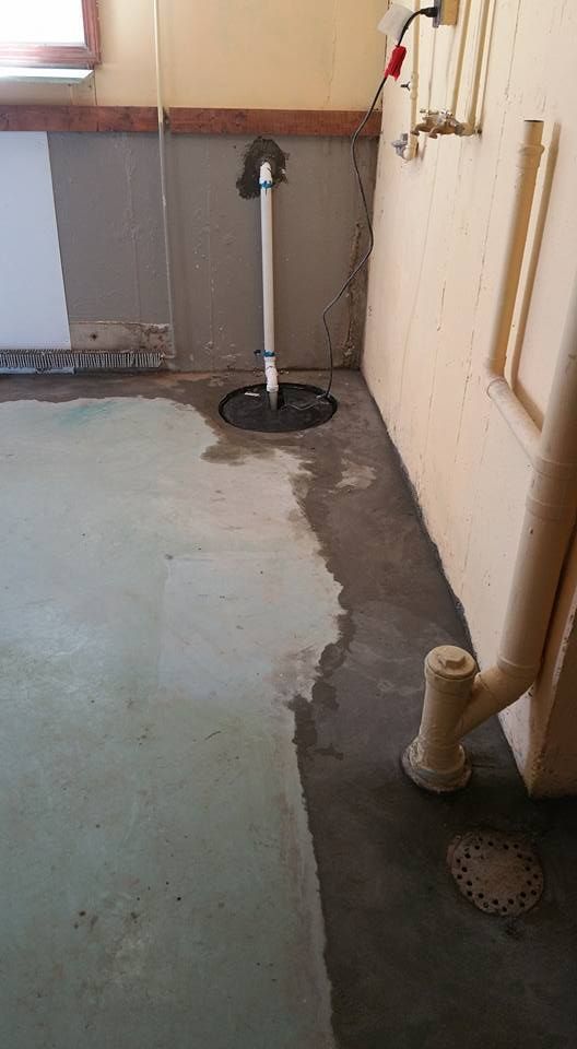 Basement corner with a sump pump, wet concrete floor, and pipes.