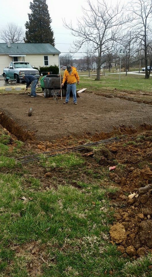 Two people preparing a garden bed outdoors. One uses a wheelbarrow.