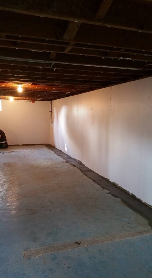 Basement with white walls, concrete floor, and wooden beams.