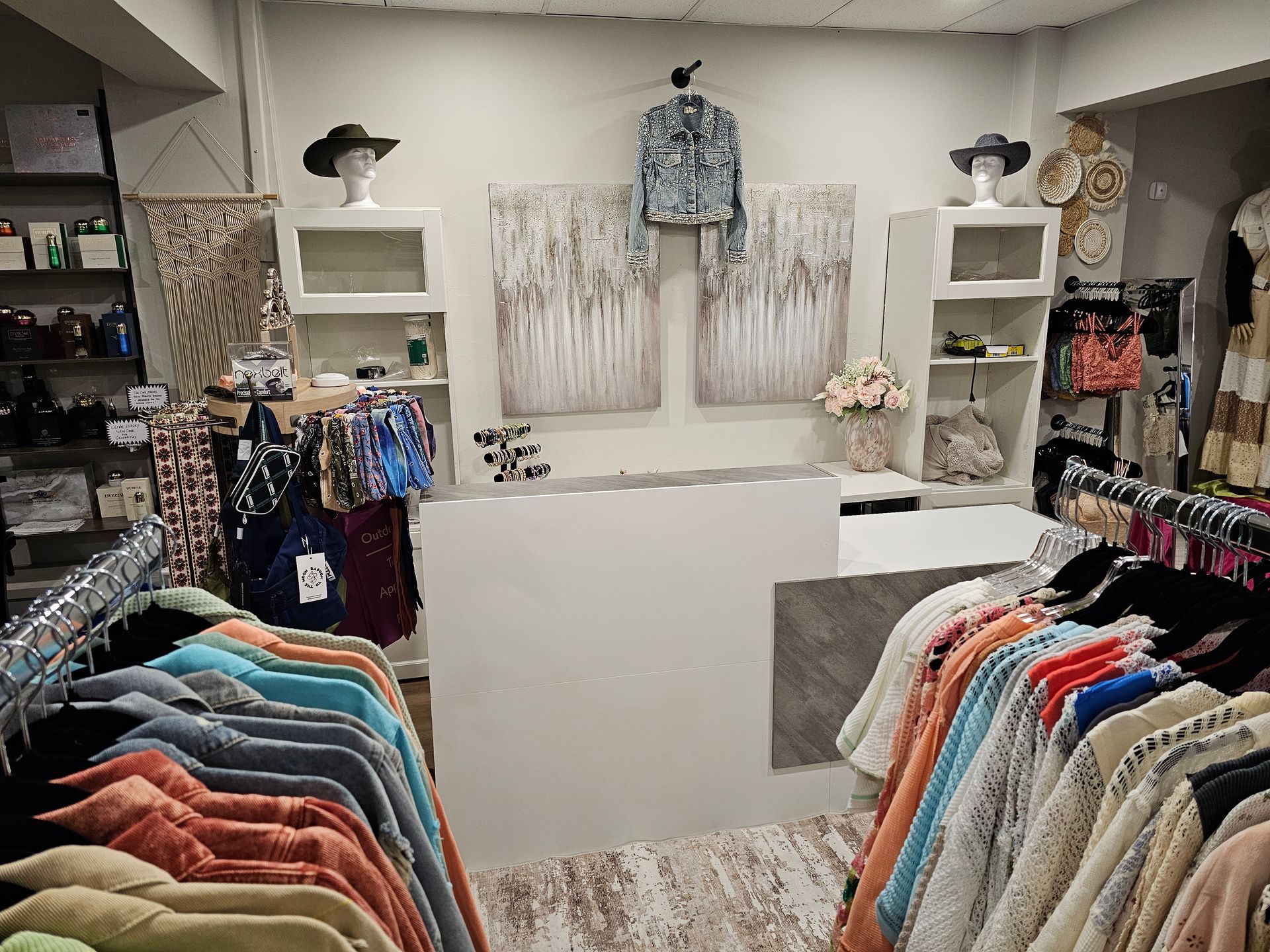Clothing store interior with clothing racks on wooden floor. Light, floral decor on walls and ceiling.