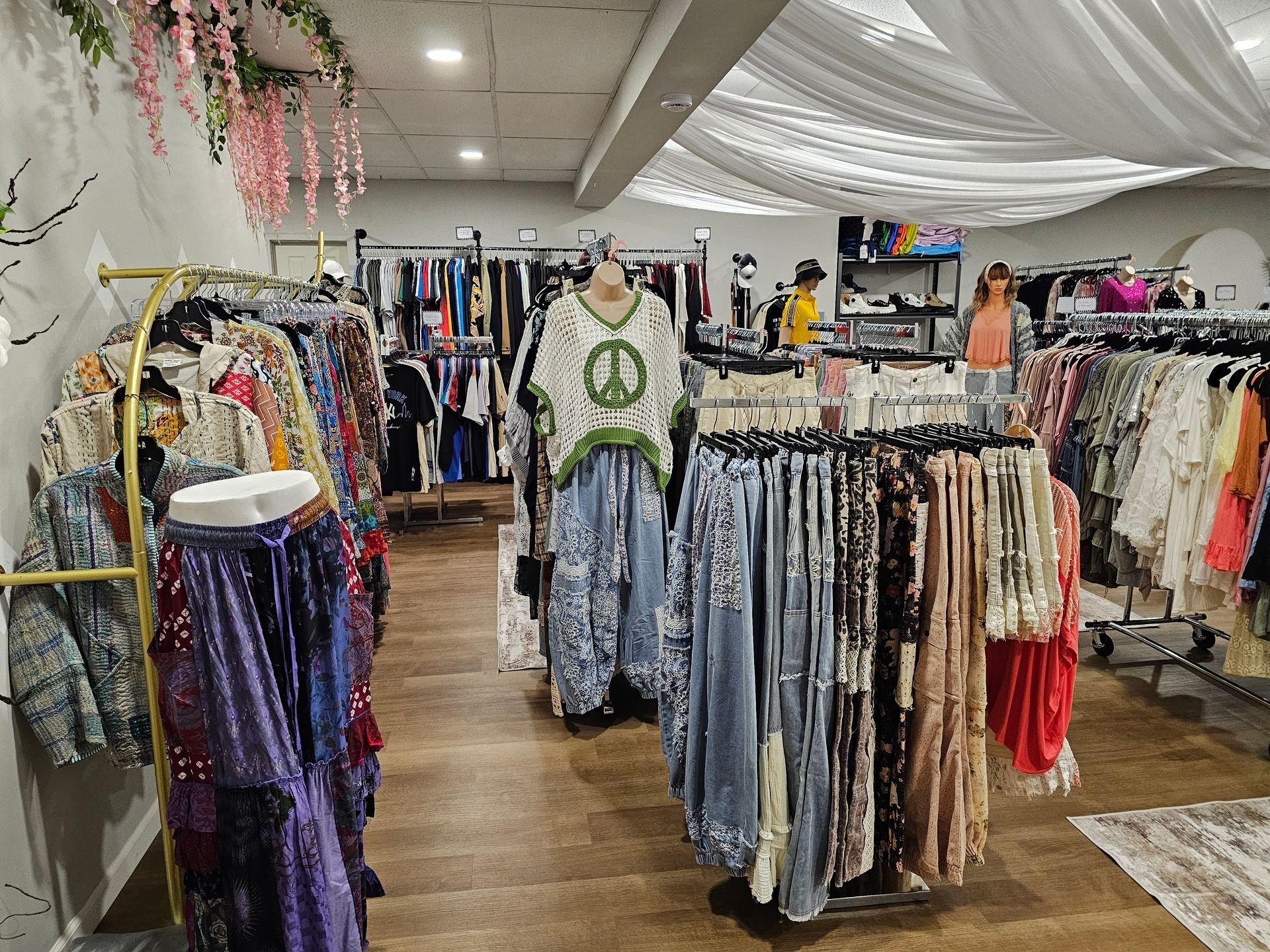 Clothing boutique interior with racks of colorful apparel, including a mannequin wearing a green peace sign top.
