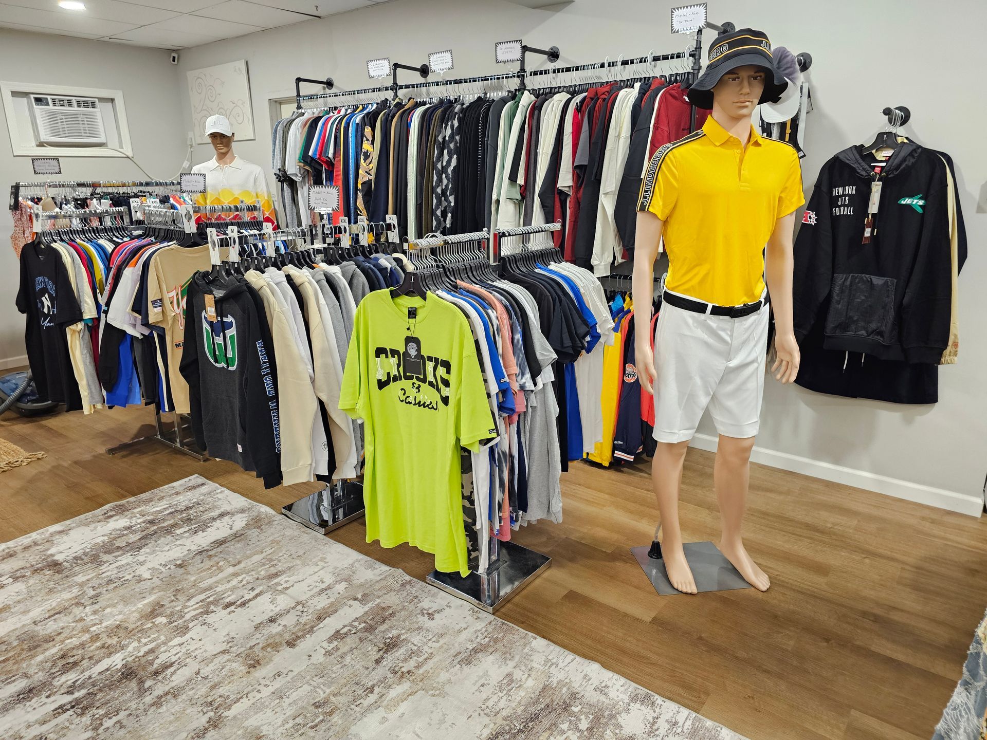 A clothing store interior featuring rows of apparel on racks and mannequins wearing a yellow polo and a white shirt.