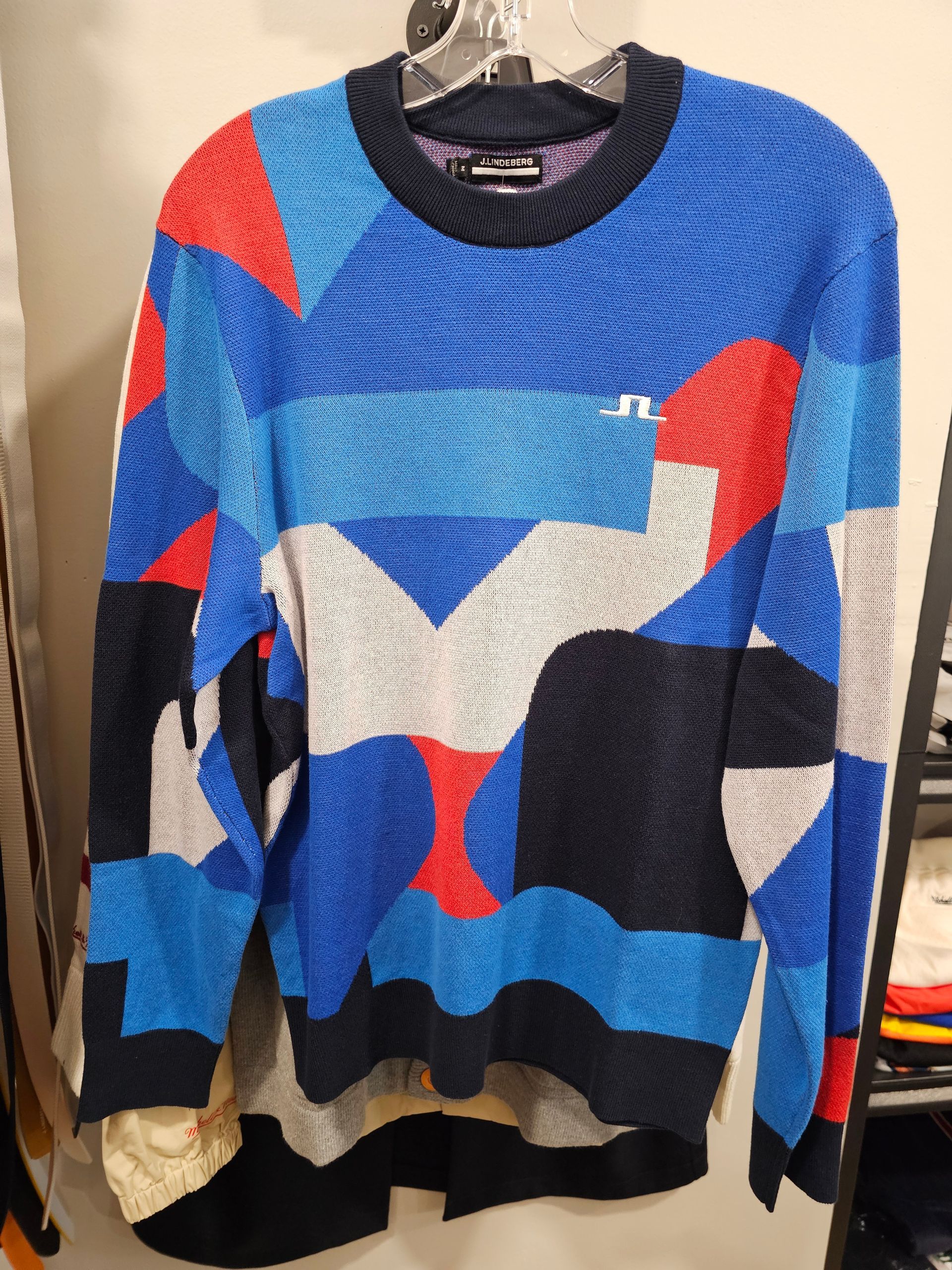 A long-sleeved sweater featuring a textured, geometric pattern in shades of blue, red, dark navy, and light grey.