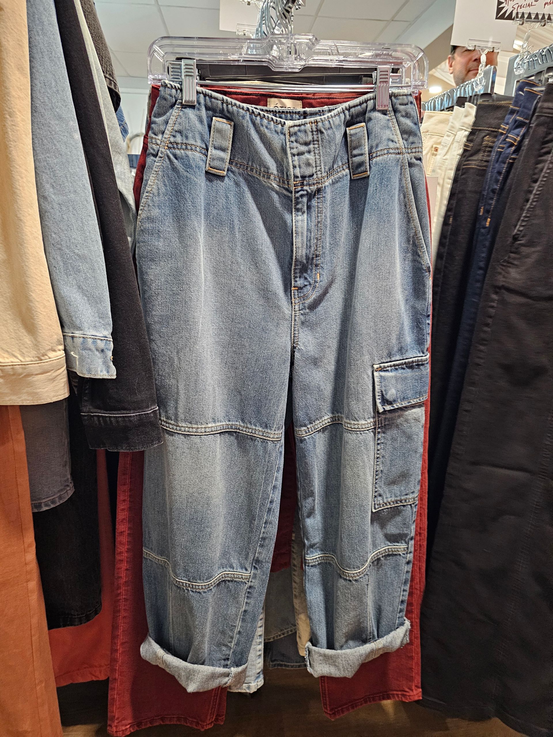 Light-wash denim cargo pants with distressed horizontal seams hanging on a clothing rack in a store.