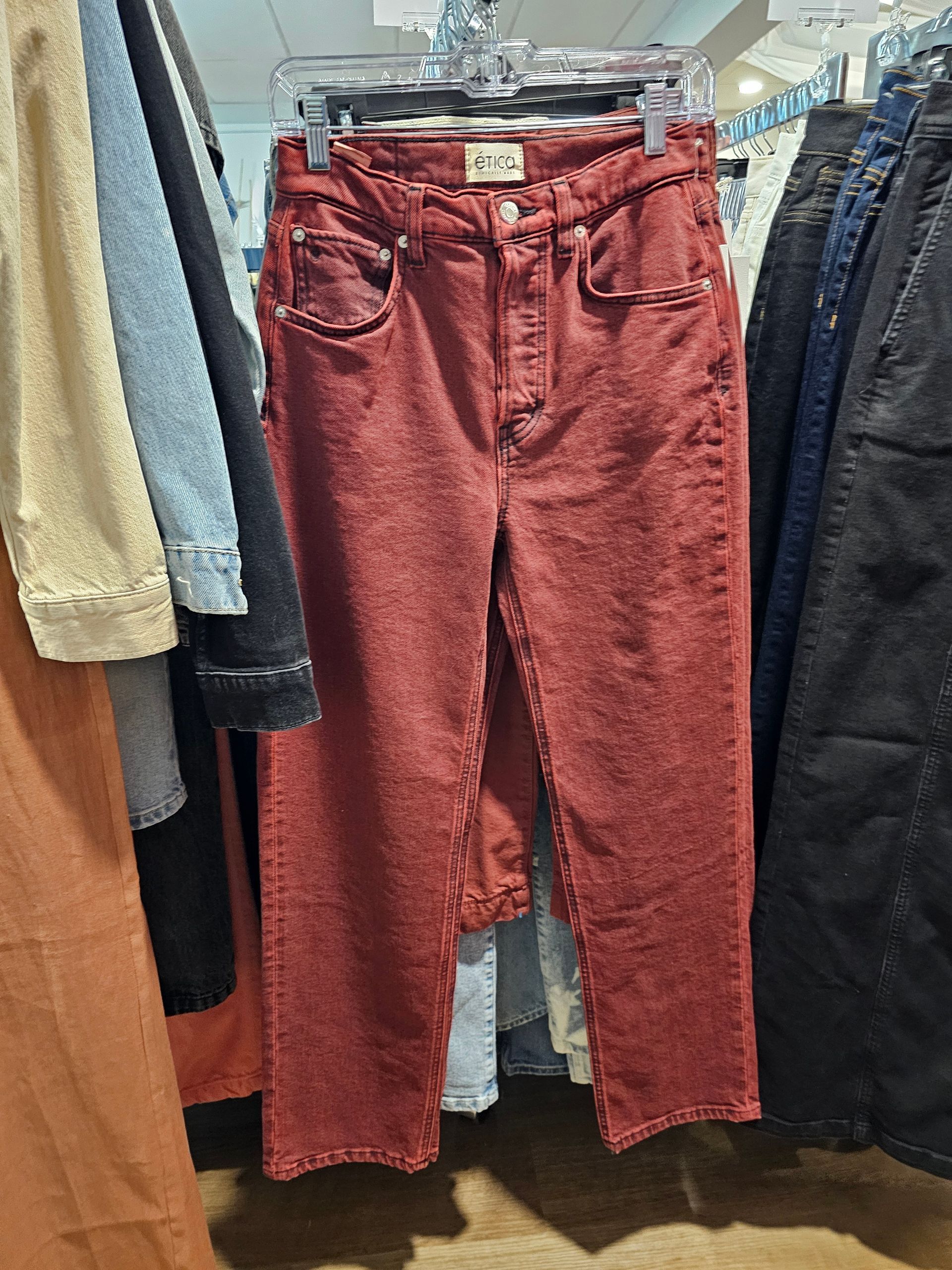 A pair of rust-colored, high-waisted denim jeans hanging on a rack in a retail store.