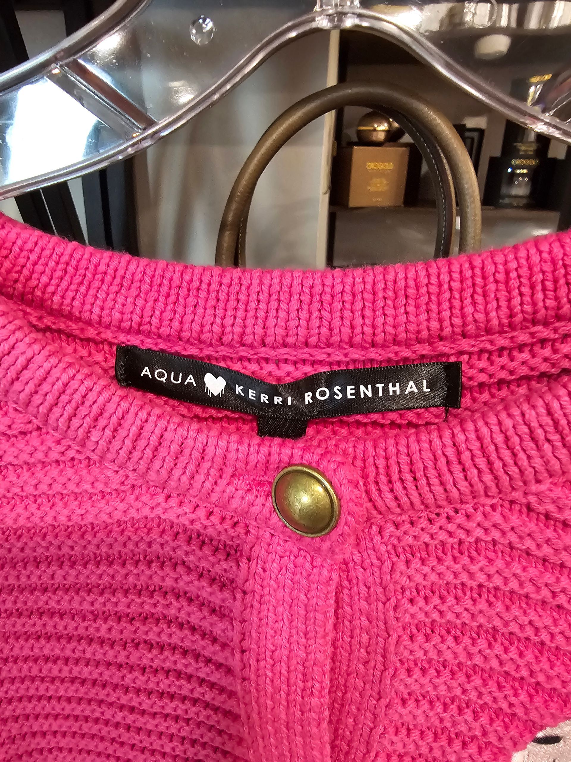 Close-up of a bright pink, textured knit cardigan with a black 