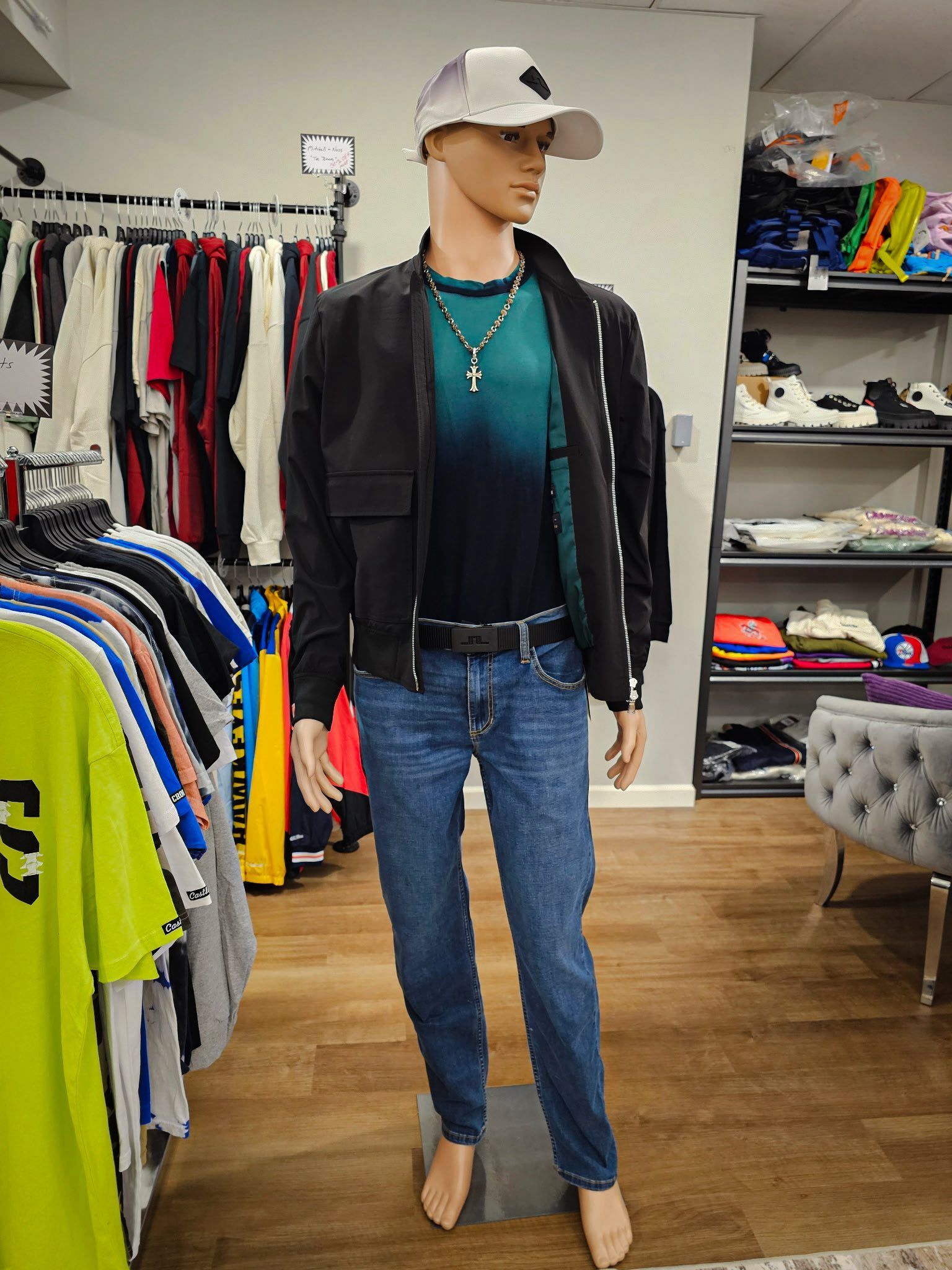Mannequin wearing a bomber jacket, jeans, and a baseball cap in a clothing store.
