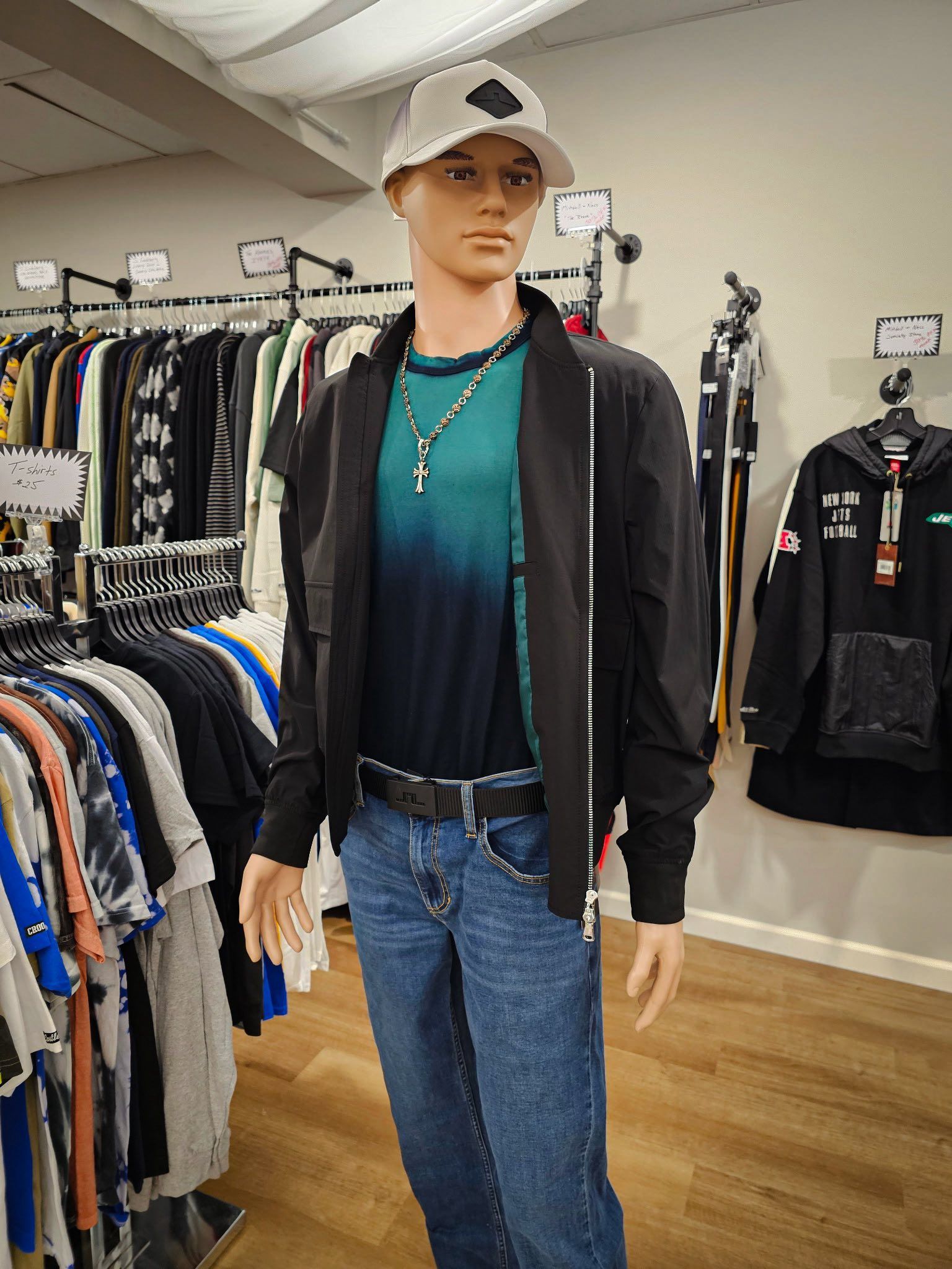 Mannequin in a clothing store, wearing a baseball cap, jacket, jeans, and a t-shirt.