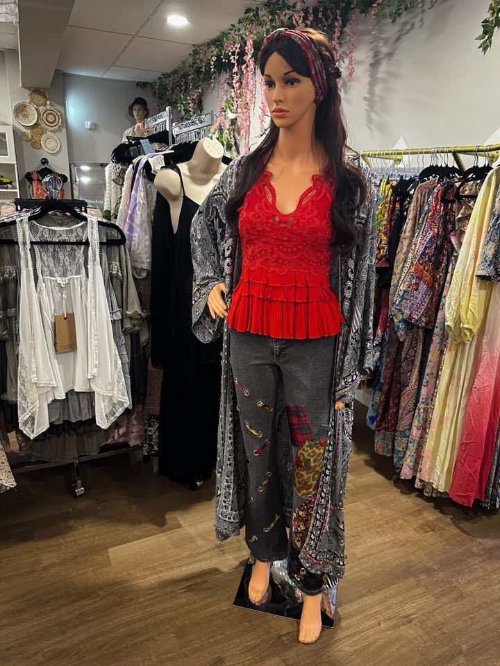 Mannequin in a store wearing a red top, jeans, and a patterned kimono. Clothing racks in the background.