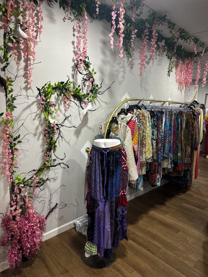 Clothing rack in a boutique with floral wall decorations. Dresses, skirts on display; wood floor.