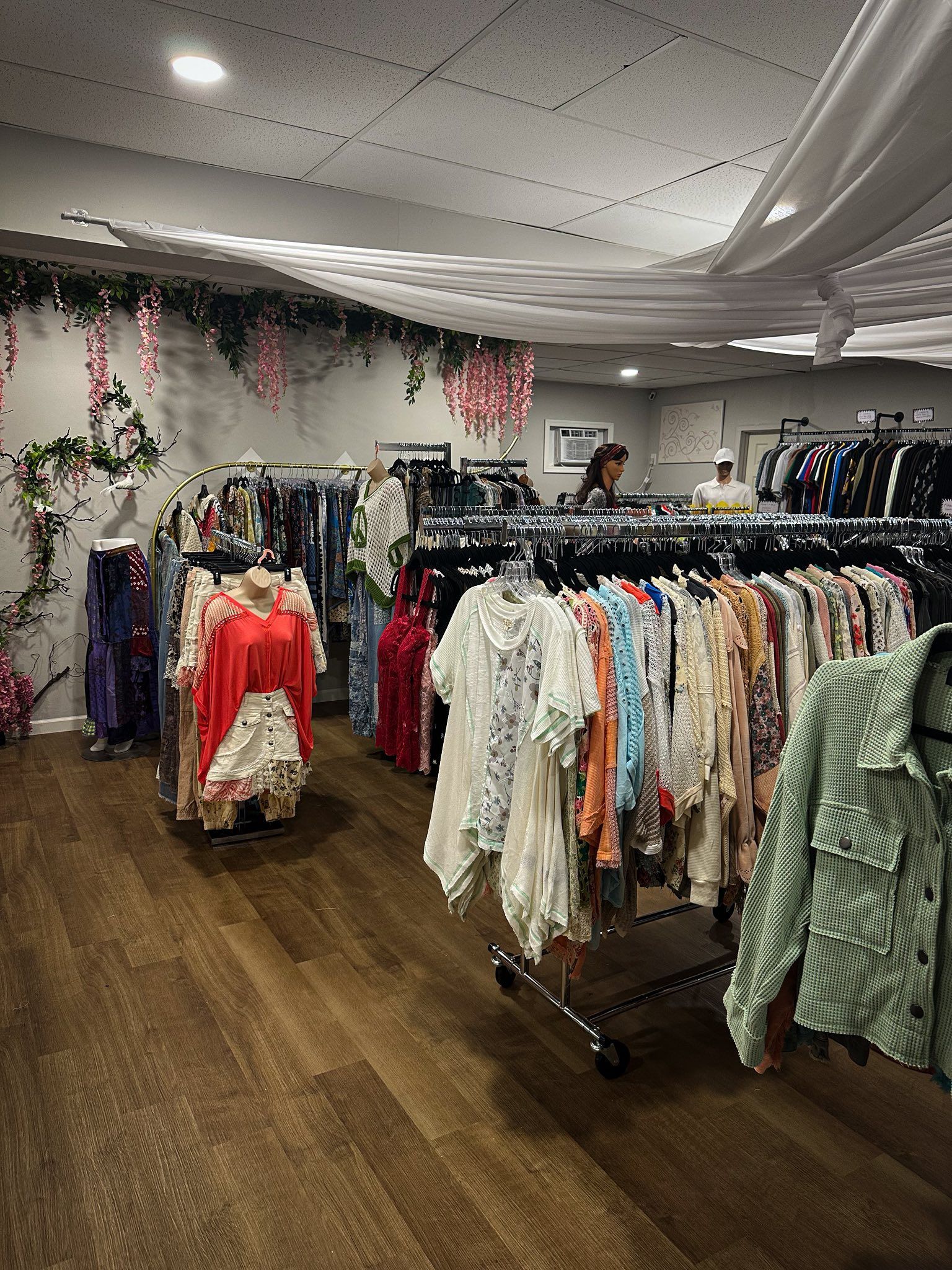 Clothing racks in a boutique, with wood floors and decorative floral accents on the walls.