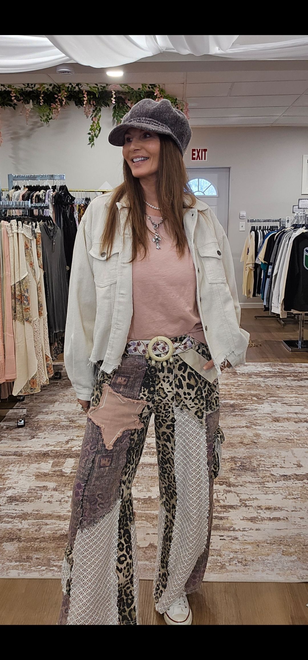 Woman in white jacket and patterned pants smiles in a clothing store.