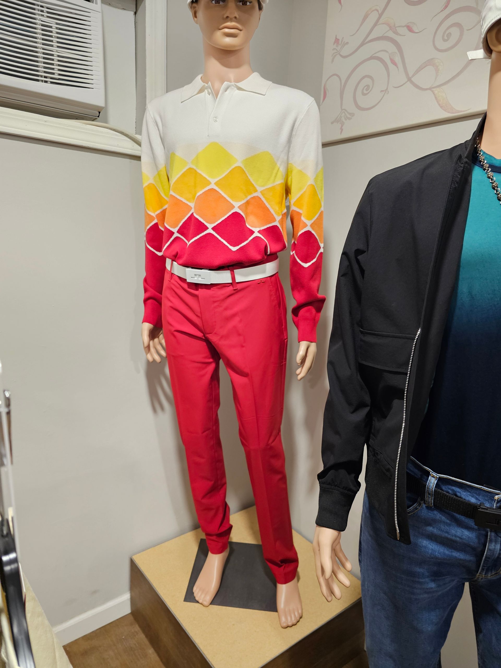 Woman in golf attire sits on green, next to a golf club and ball. She wears a red shirt, shorts, bucket hat, and black shoes.