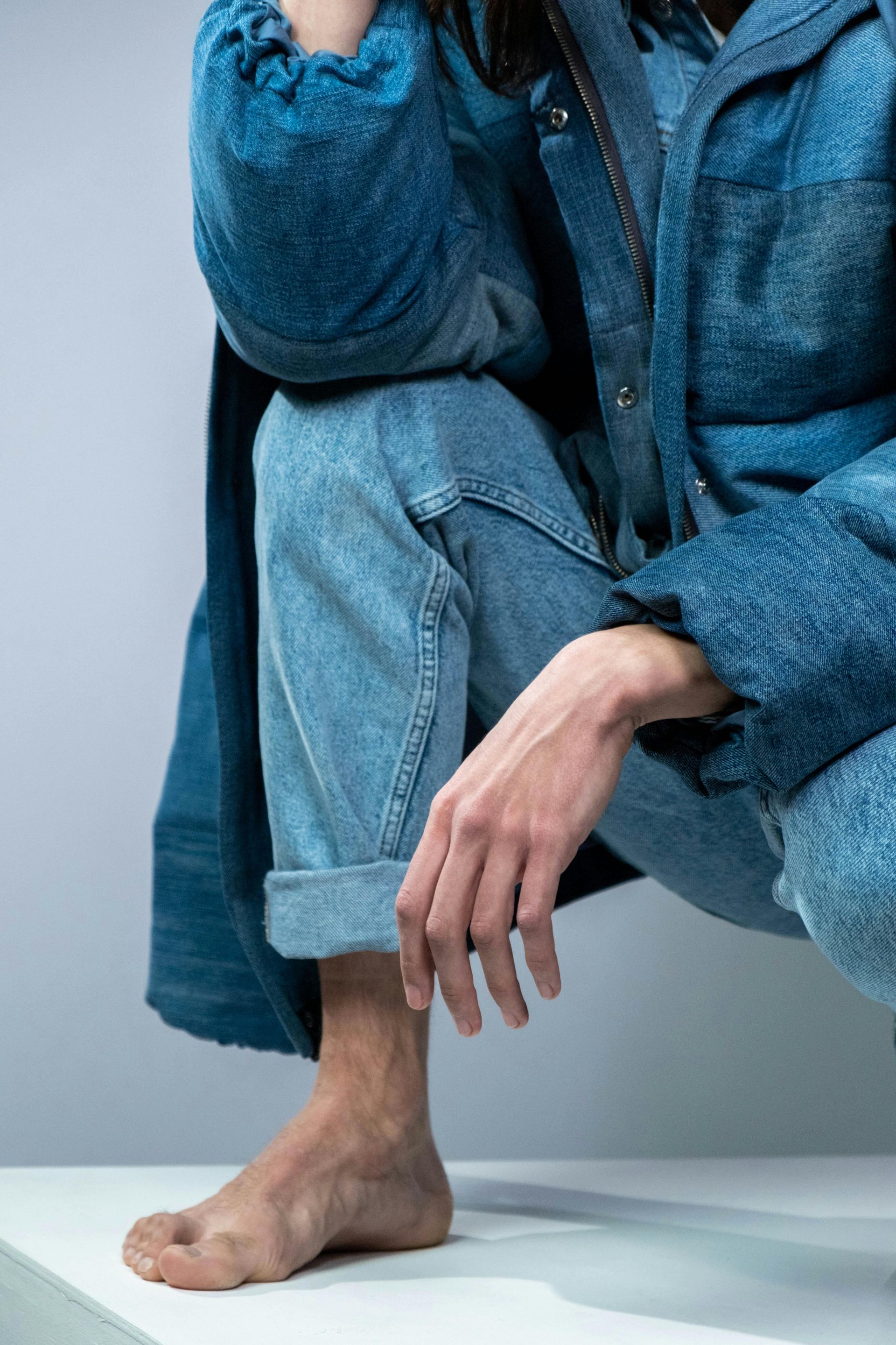 Person in denim jacket and jeans, crouching barefoot.