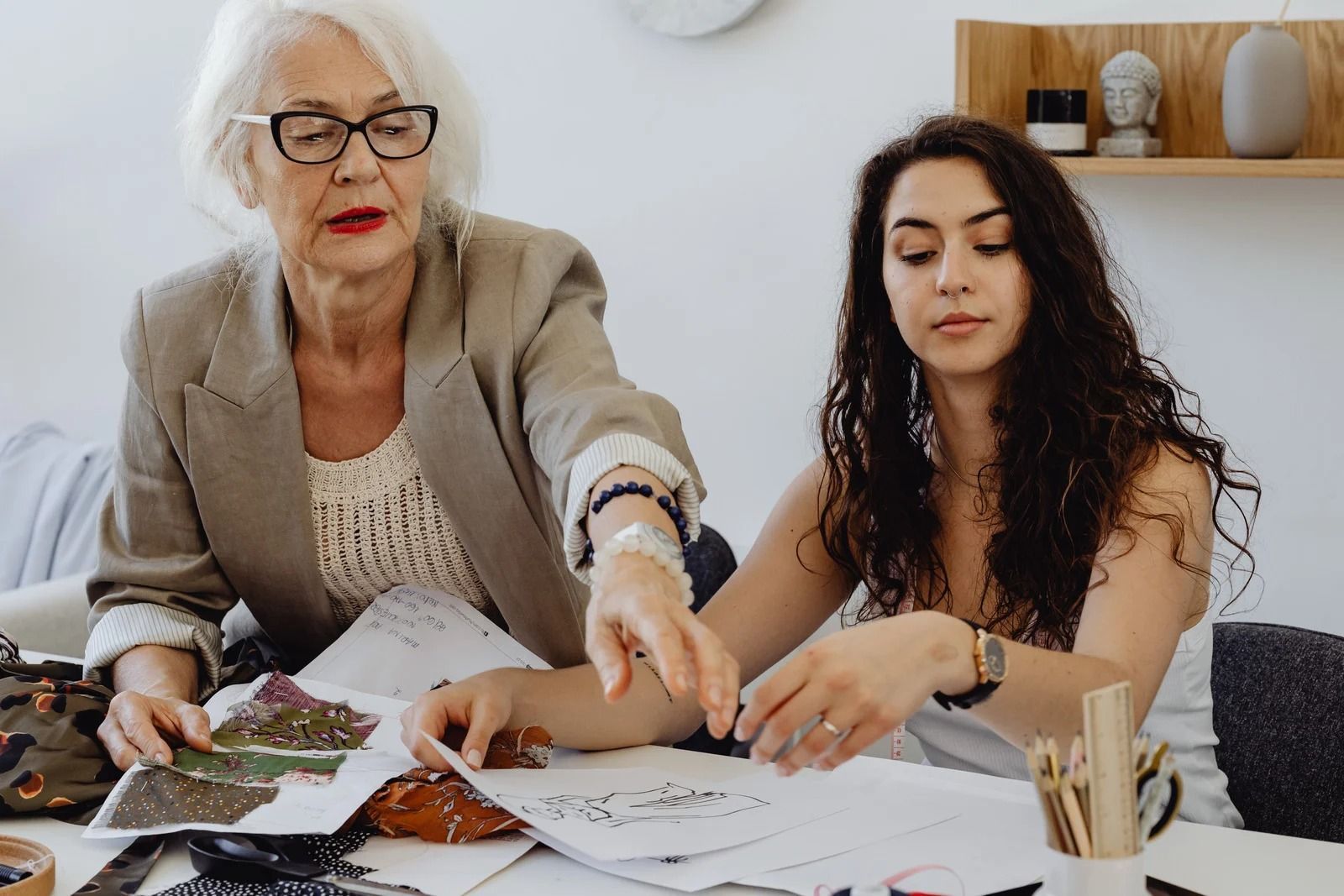Two people sit at a table reviewing sketches and fabric swatches in a well-lit workspace.