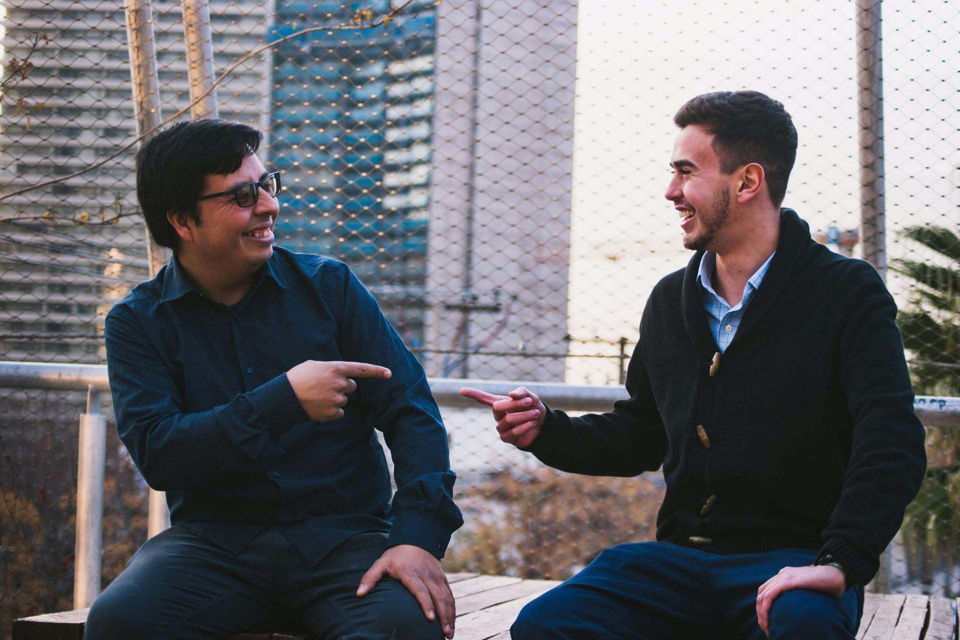 Two men are sitting on a bench talking to each other.