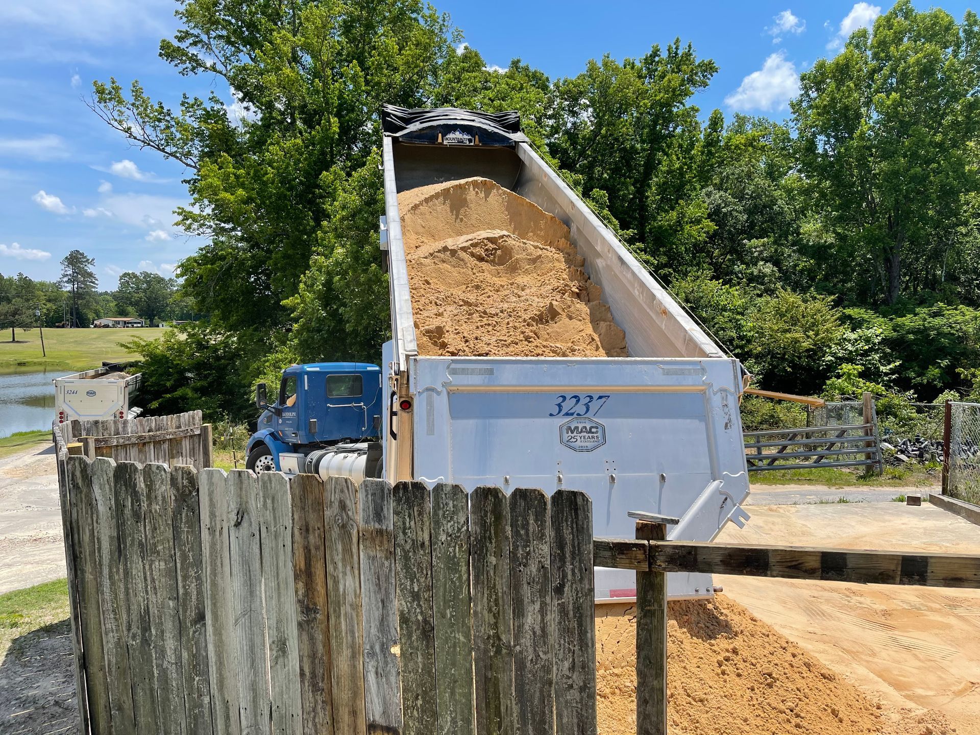 Dump truck unloading rocks. The truck is white, with the bed raised. Rocks and dirt in the background.