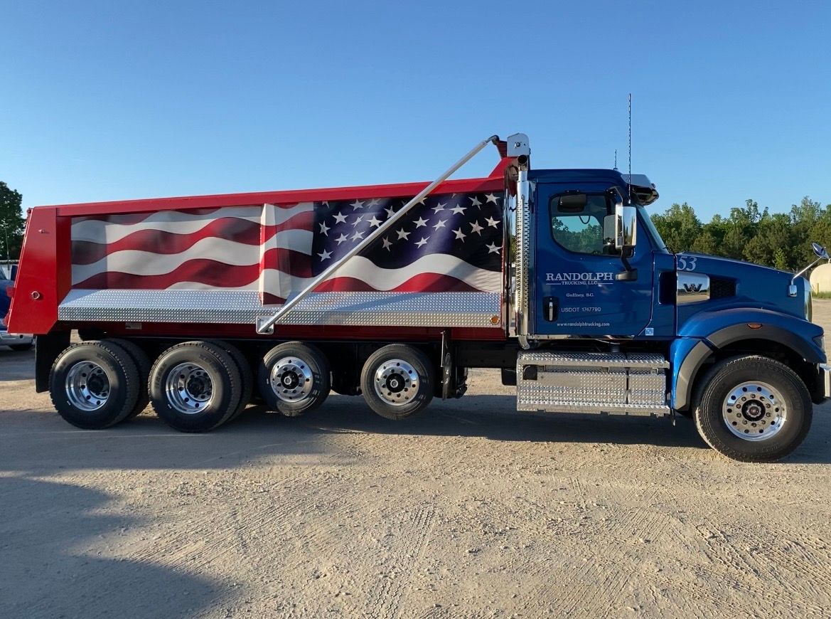 Man in black polo shirt stands by a blue semi-truck with 