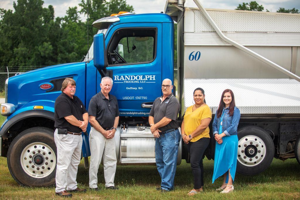 Man in black polo shirt stands by a blue semi-truck with