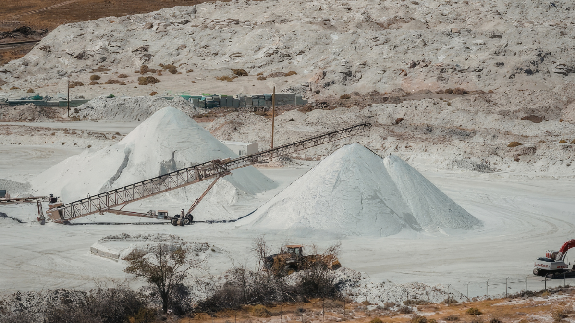 White piles of mined material, conveyor belt, and industrial equipment at an outdoor quarry.