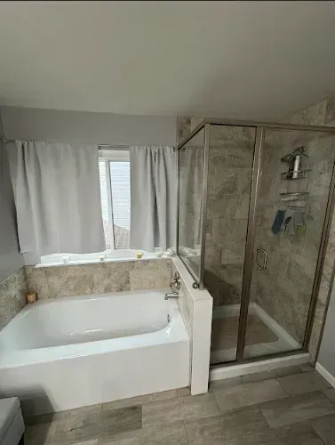 Bathroom with a white bathtub, glass shower, light gray walls, and curtained window.
