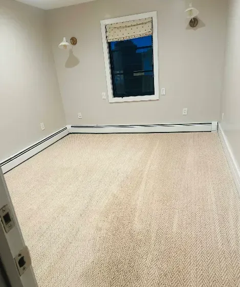 Empty room with beige carpet, light walls, window, and wall sconces.