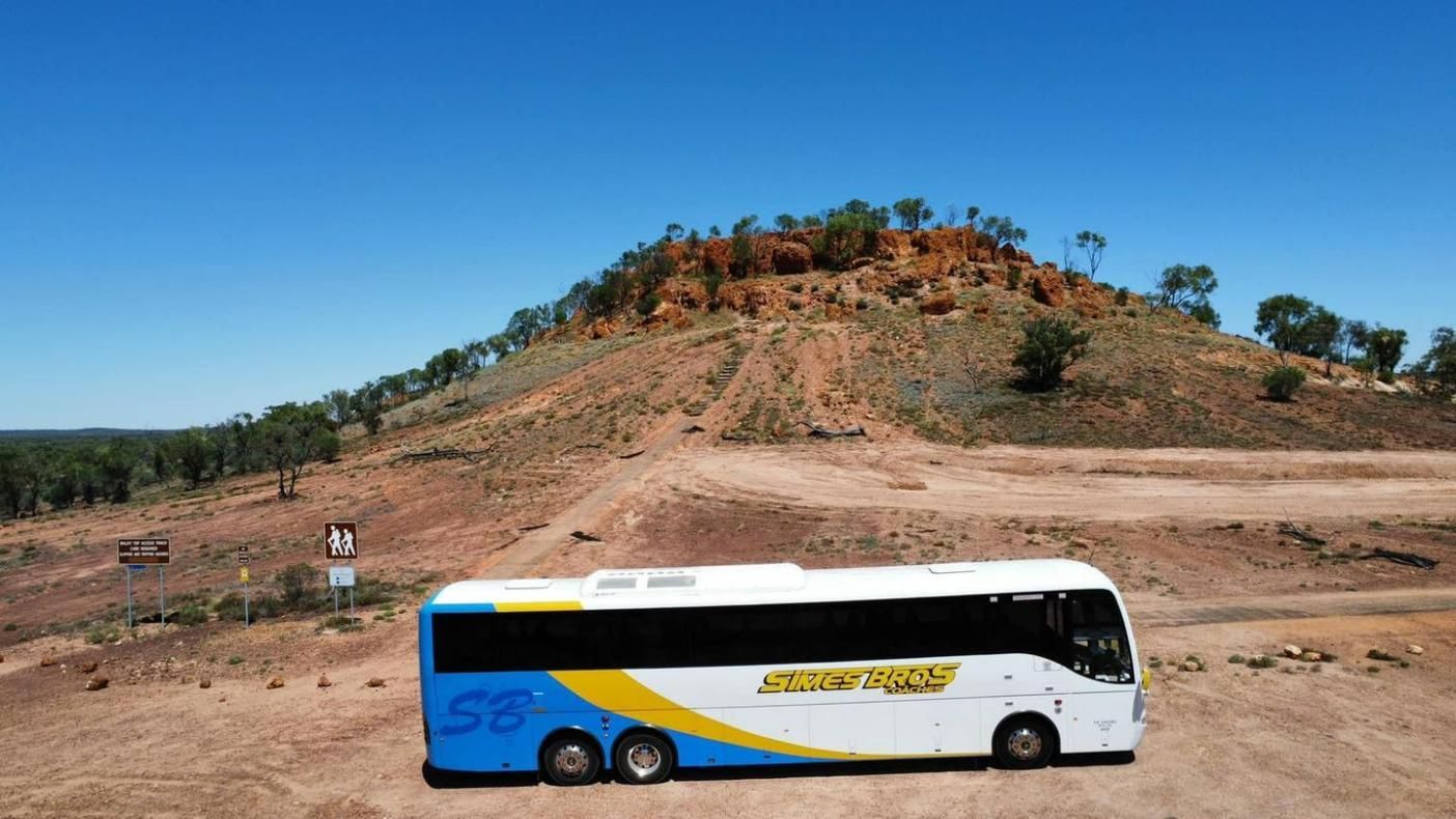 A White and Blue Bus Is Parked on The Side of A Dirt Road — Simes Bros Coaches in South Lismore, NSW