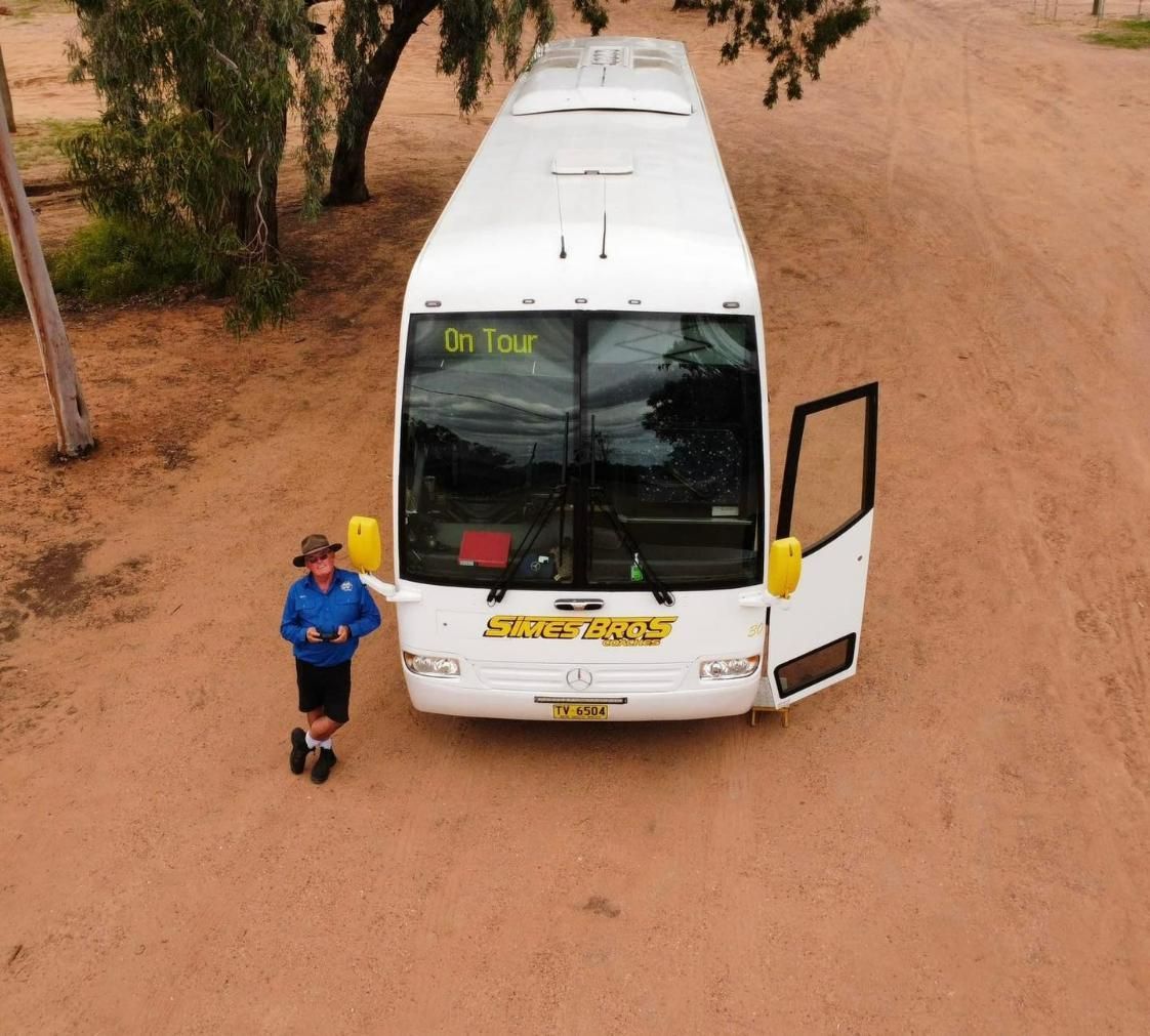 A Man Is Standing in Front of A Bus that Says On Tour — Simes Bros Coaches in South Lismore, NSW