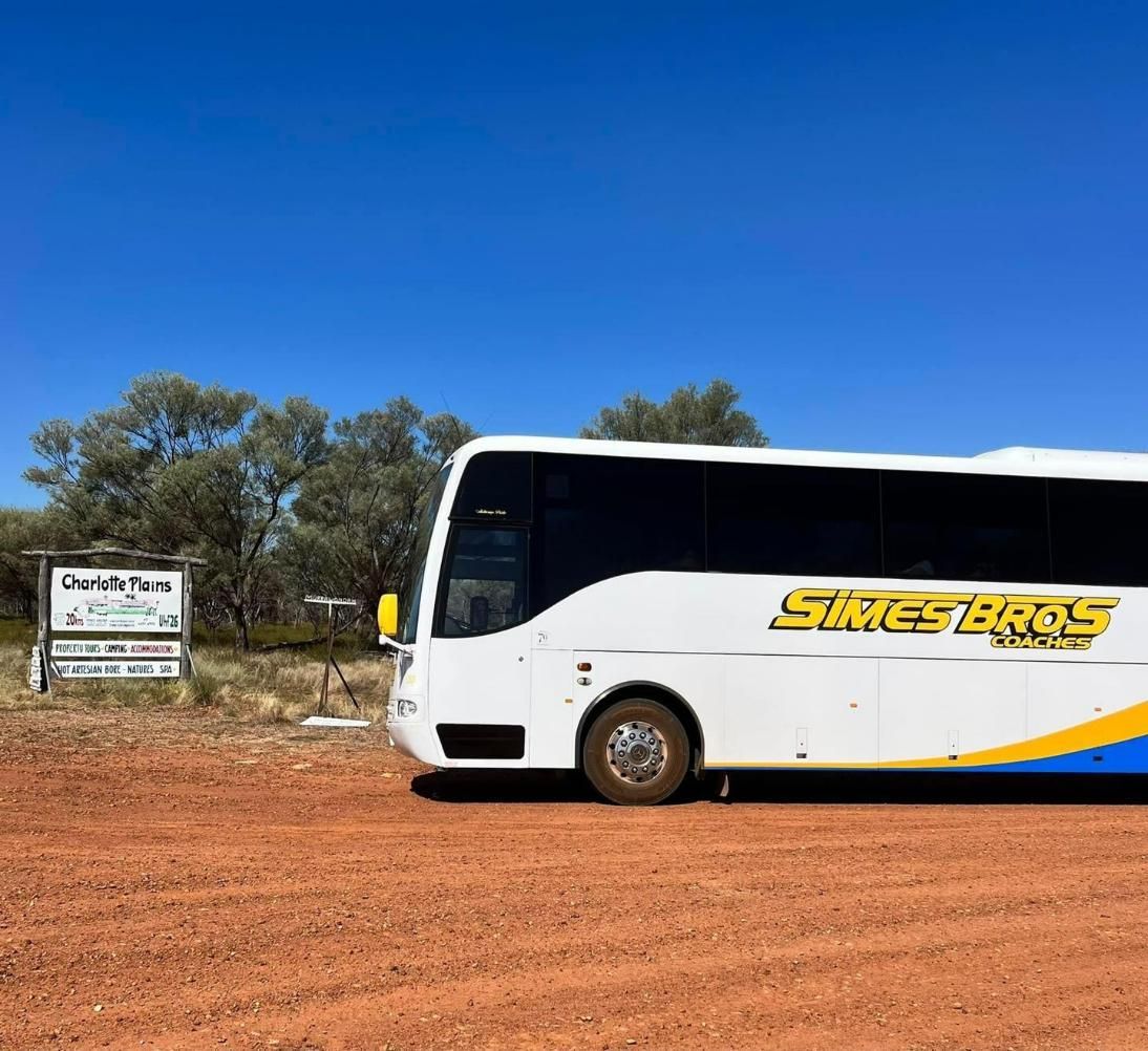 A White and Yellow Bus Is Parked in A Dirt Field — Simes Bros Coaches in South Lismore, NSW