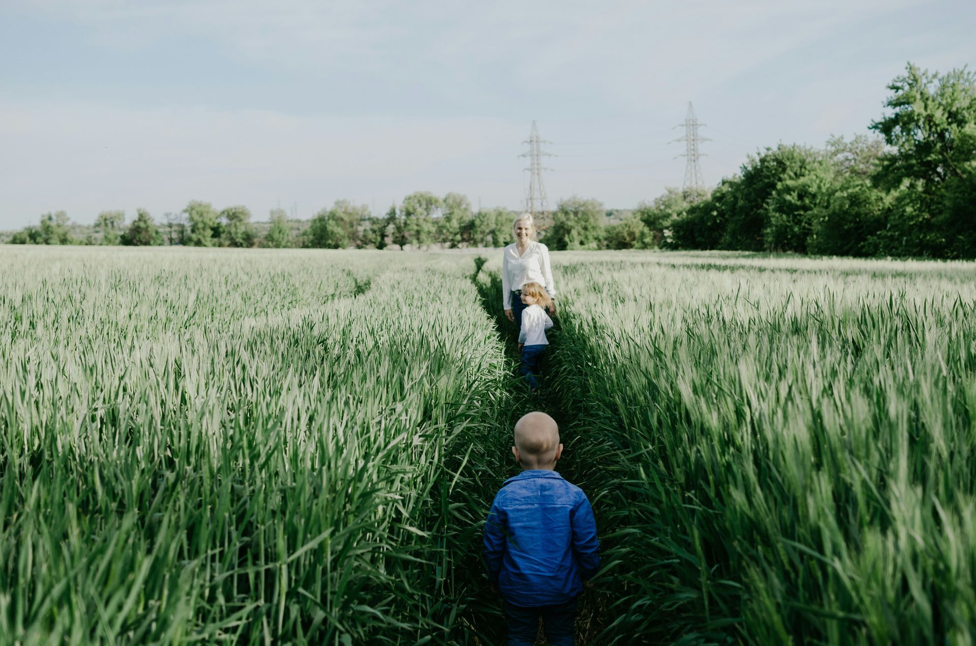 An adult walking ahead with a child following through a grassy field.