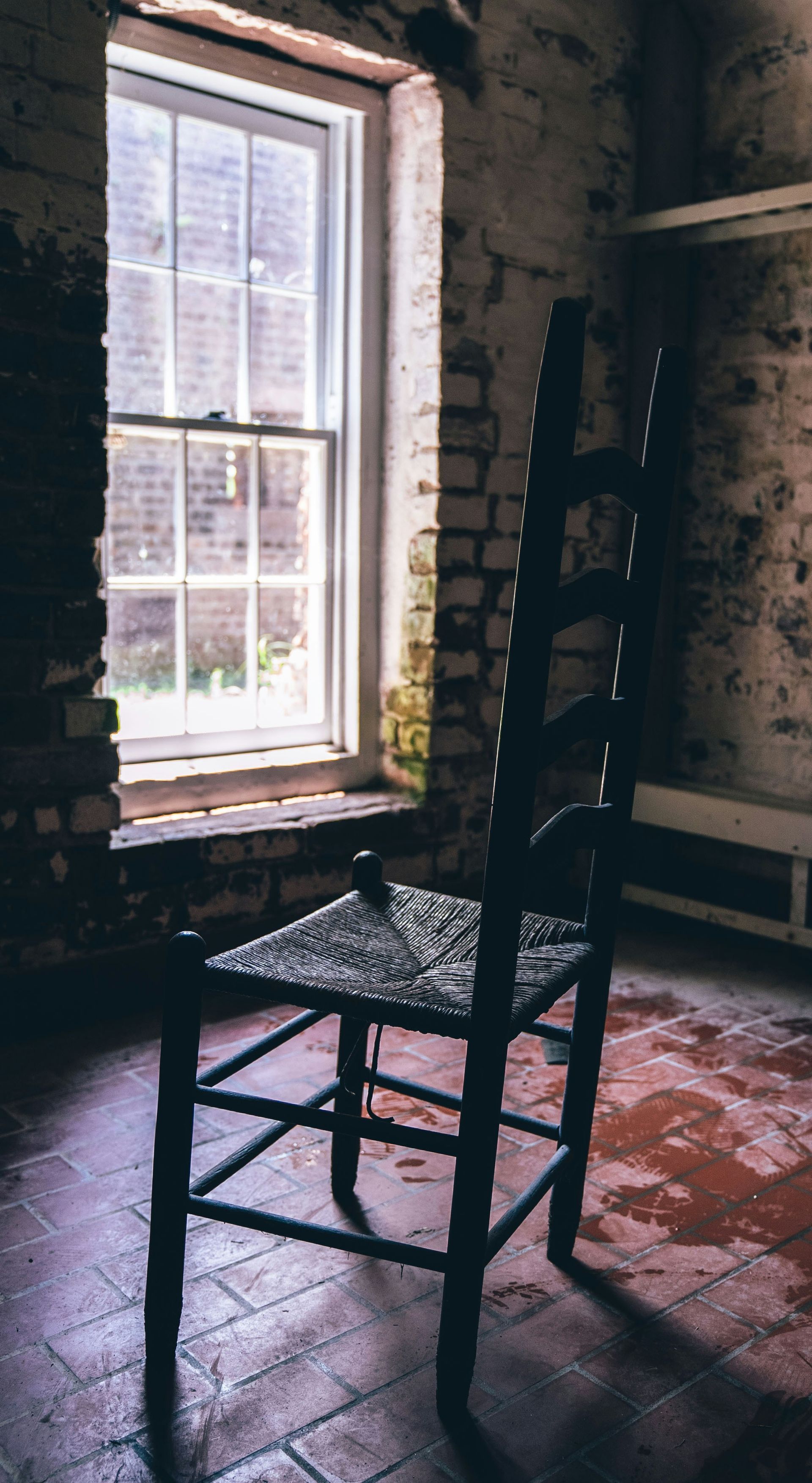An empty wooden chair beside a window in a quiet, dimly lit room, symbolizing emotional absence 