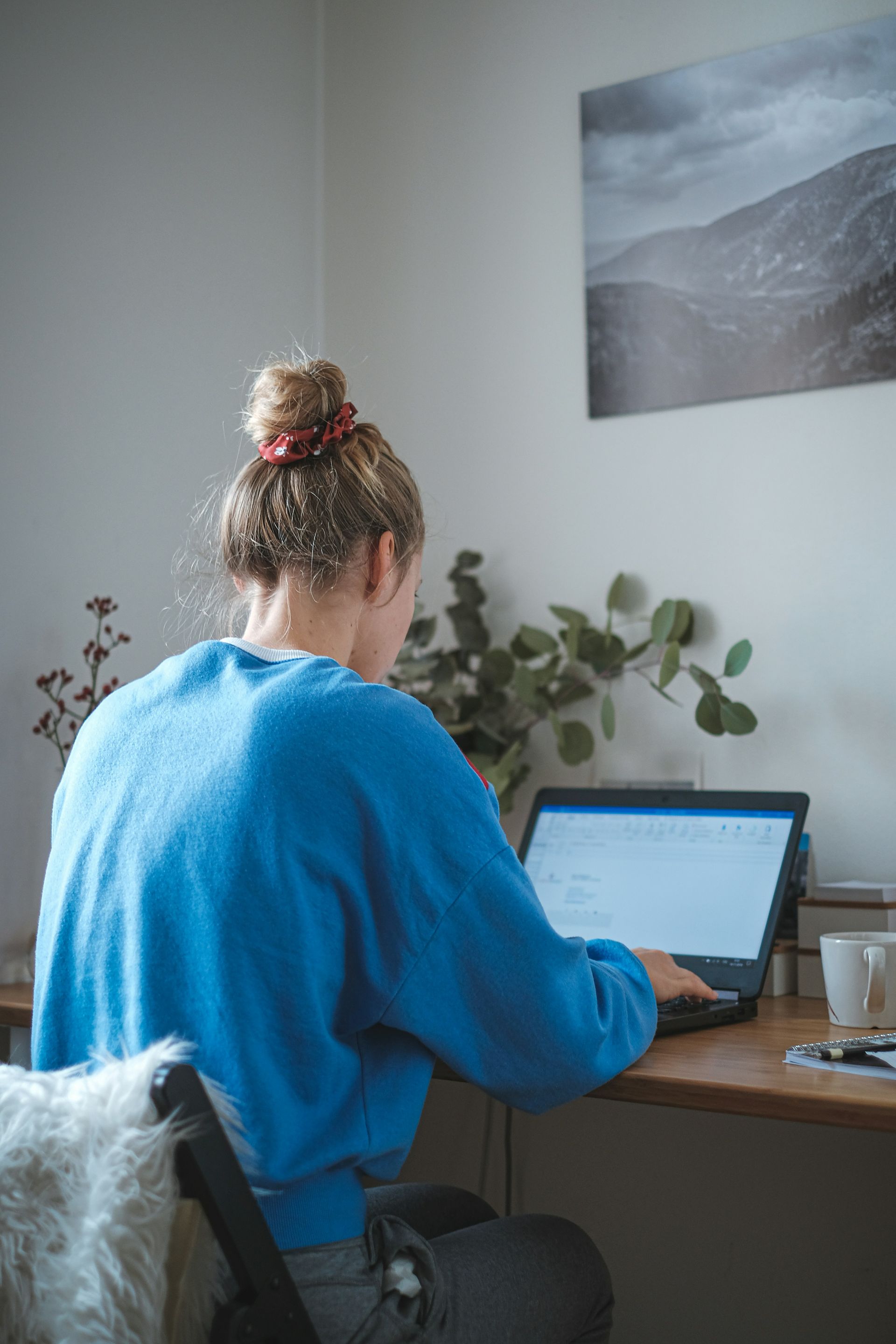 A woman sitting at a desk, looking at her laptop, working