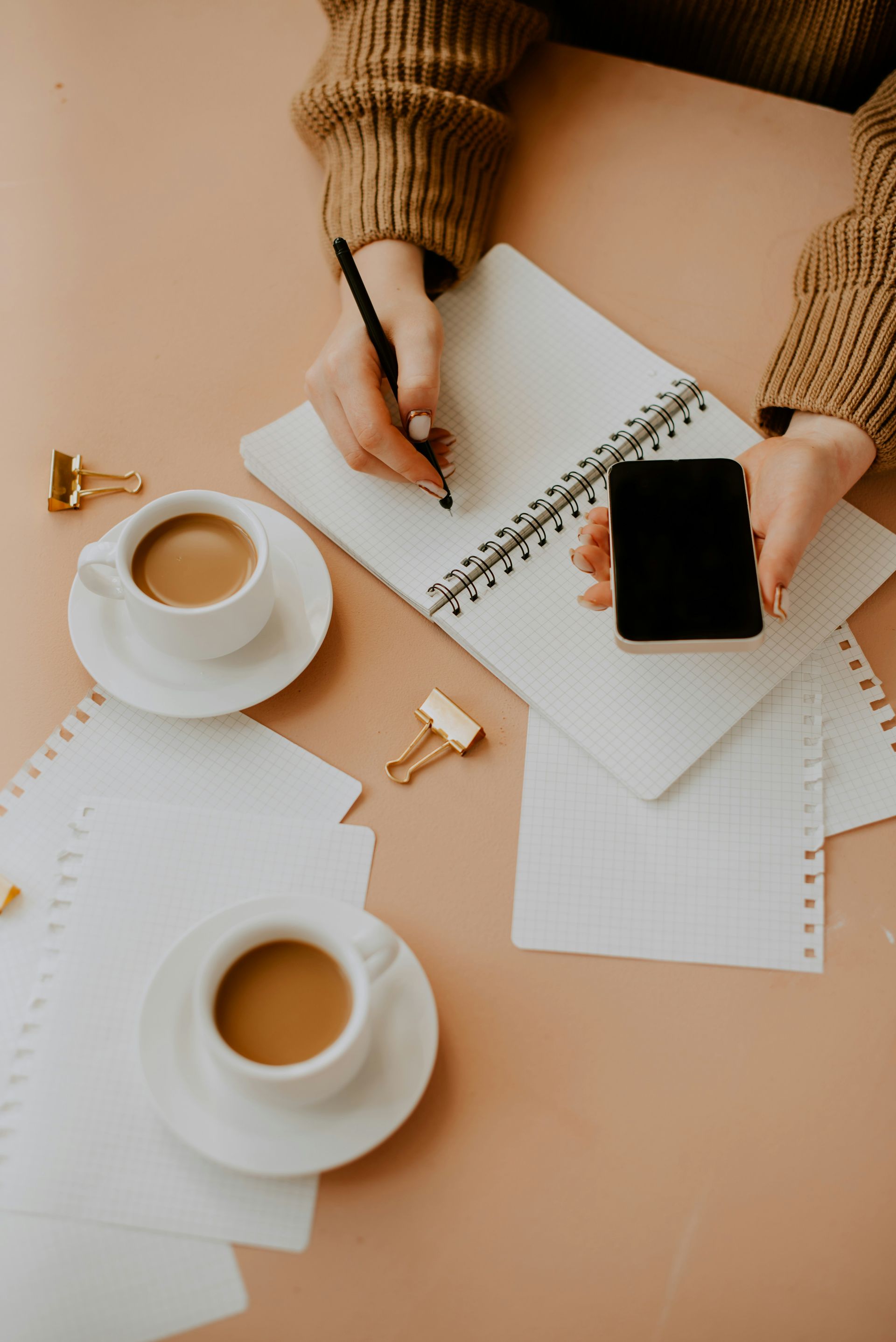 A person writing in a notebook on a desk with a cup of coffee.