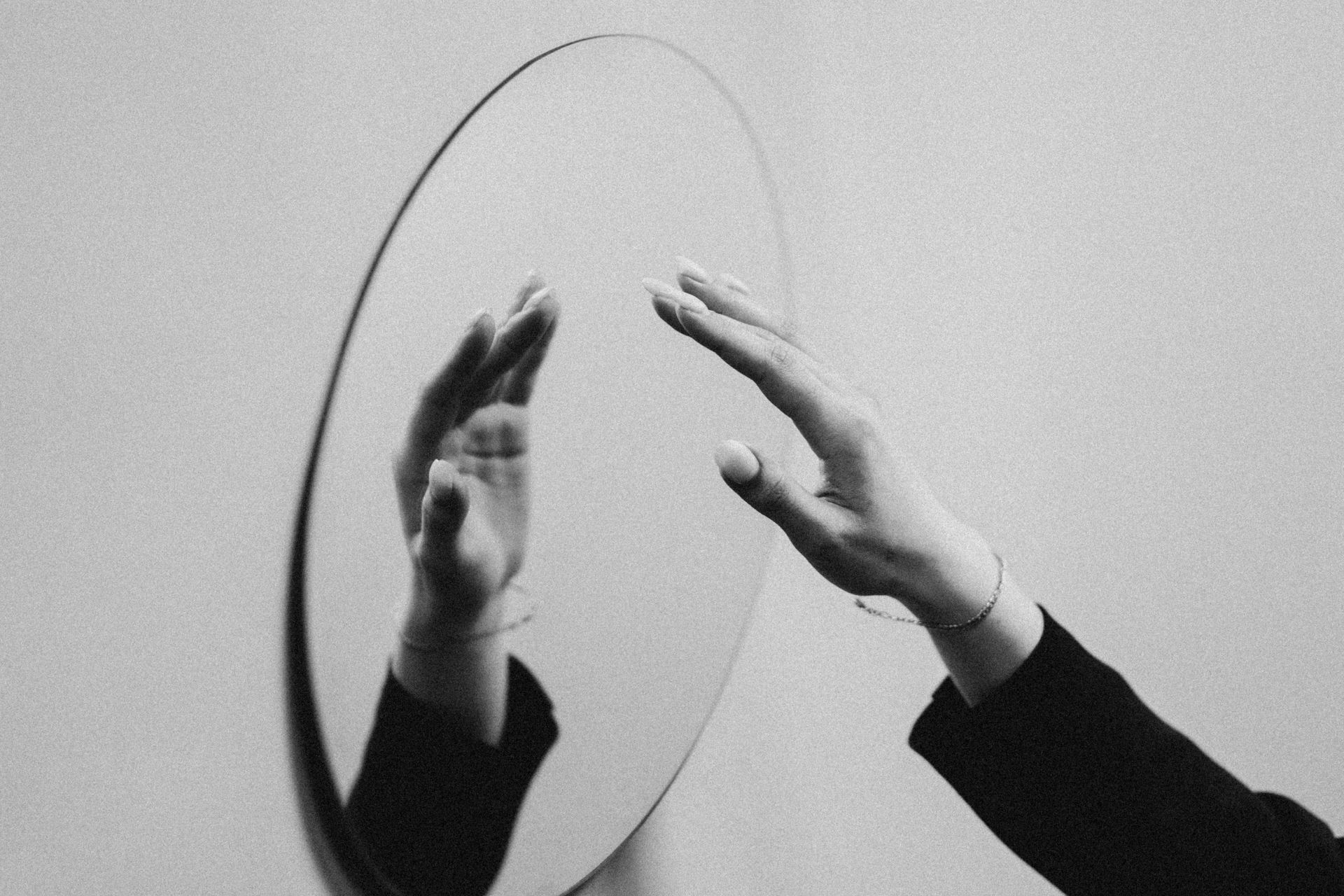 A person reaching toward their reflection in a circular mirror, symbolizing self-awareness