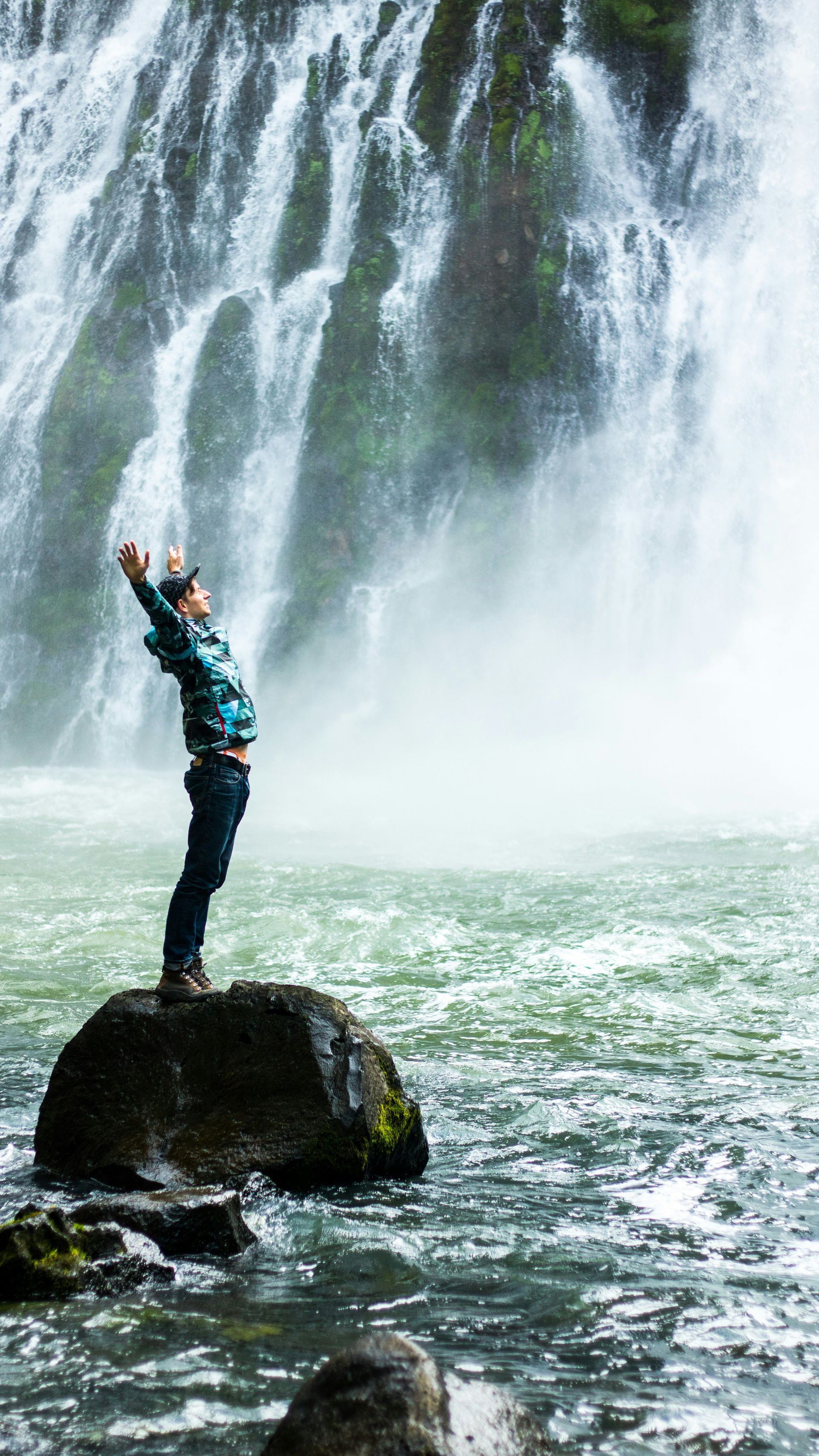 A person standing on a rock with arms open in front of a powerful waterfall, symbolizing emotional release, freedom, and stepping into a stronger version of themselves