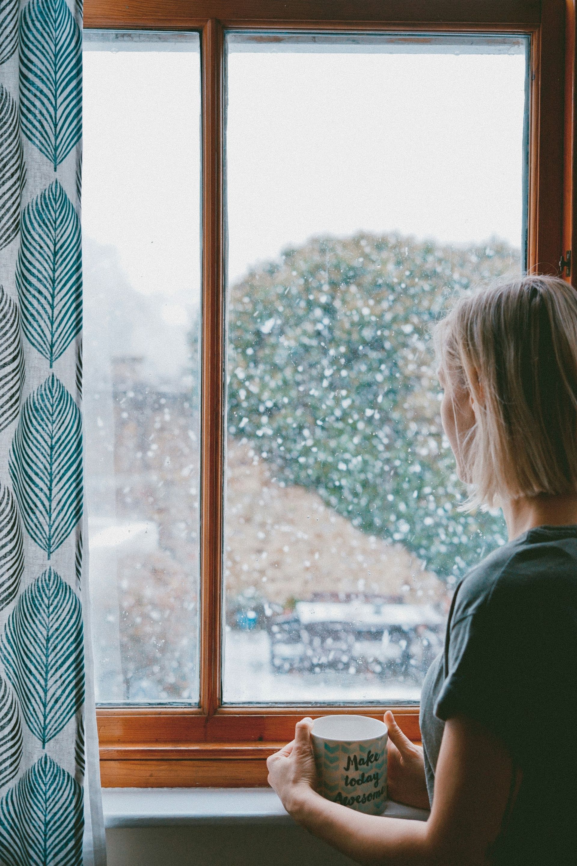 A person sitting by a window holding a mug.